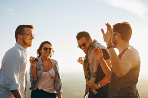 Three men and one woman stand outside in a circle and laugh