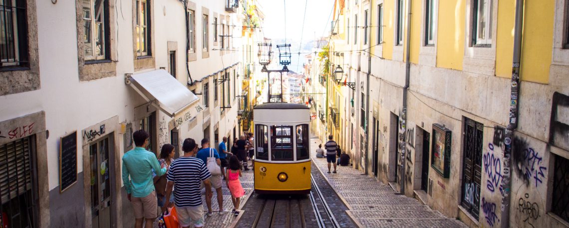 People going down a street where a metro drives in the middle