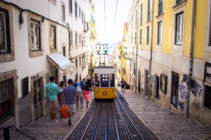 People going down a street where a metro drives in the middle