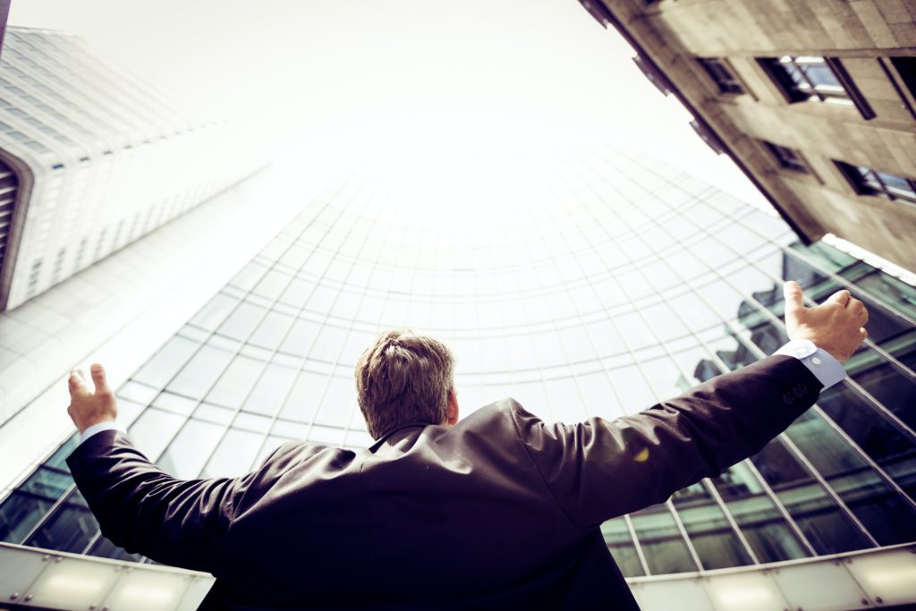 Man celebrating his success by putting his hands in the air in front of a high building