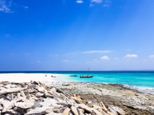 A sand beach with rocks in the front, turquoise sea water and a little boat